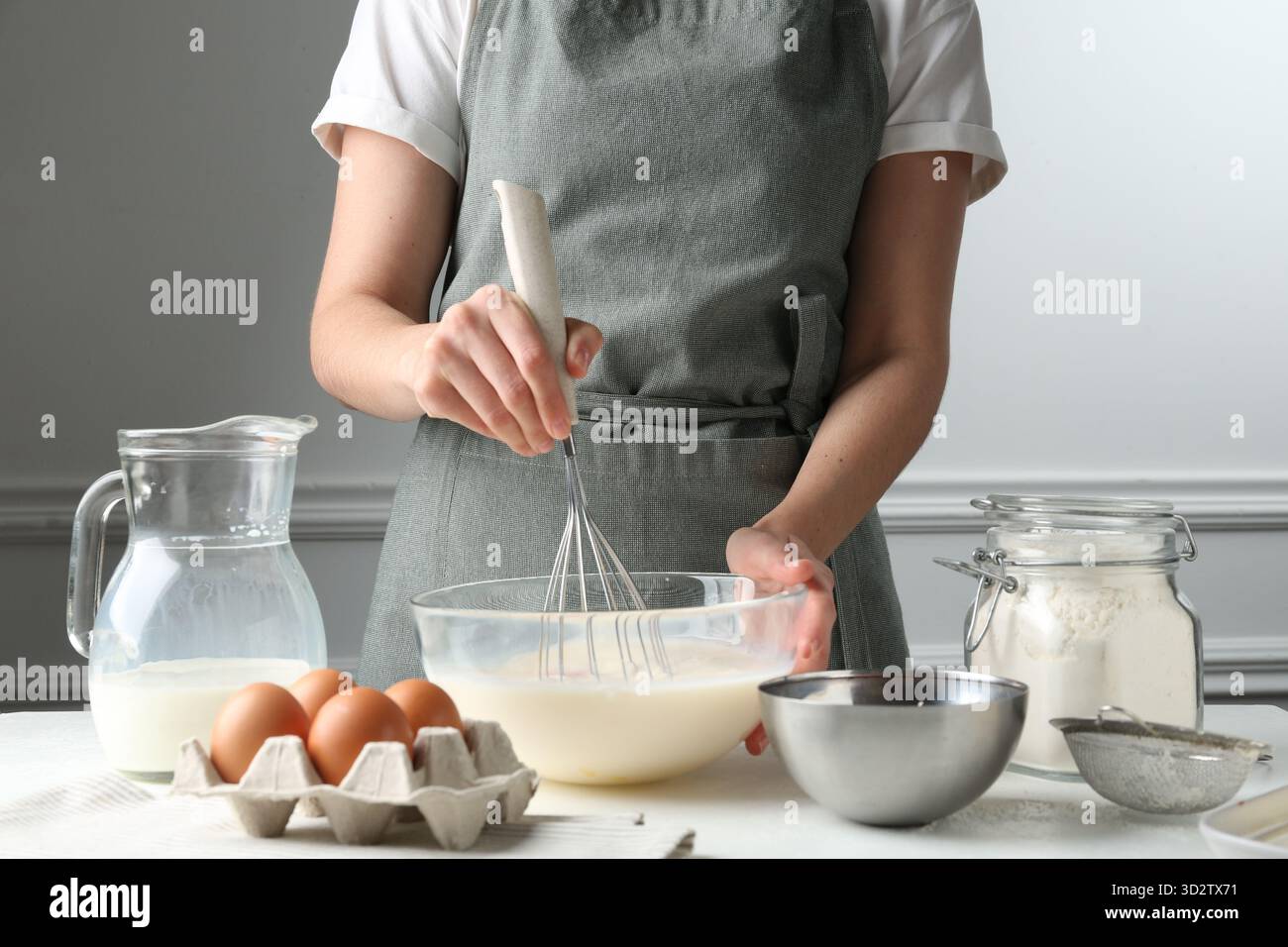 Woman making batter (liquid dough) at white table indoors, closeup ...