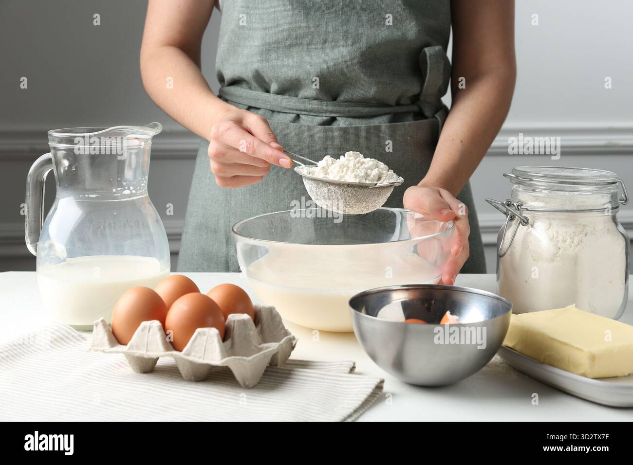 Making batter (liquid dough). Woman sieving flour into bowl at white ...