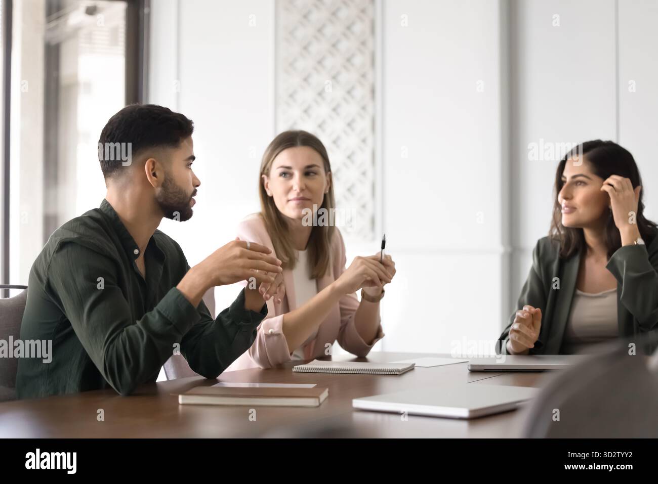Three professionals engaged in brainstorming session, focused conversation at table Stock Photo
