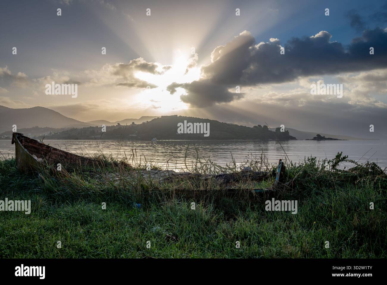 An Autumnal seascape at dawn with sun rays breaking through the clouds, and a broken wooden boat in the foreground. Stock Photo