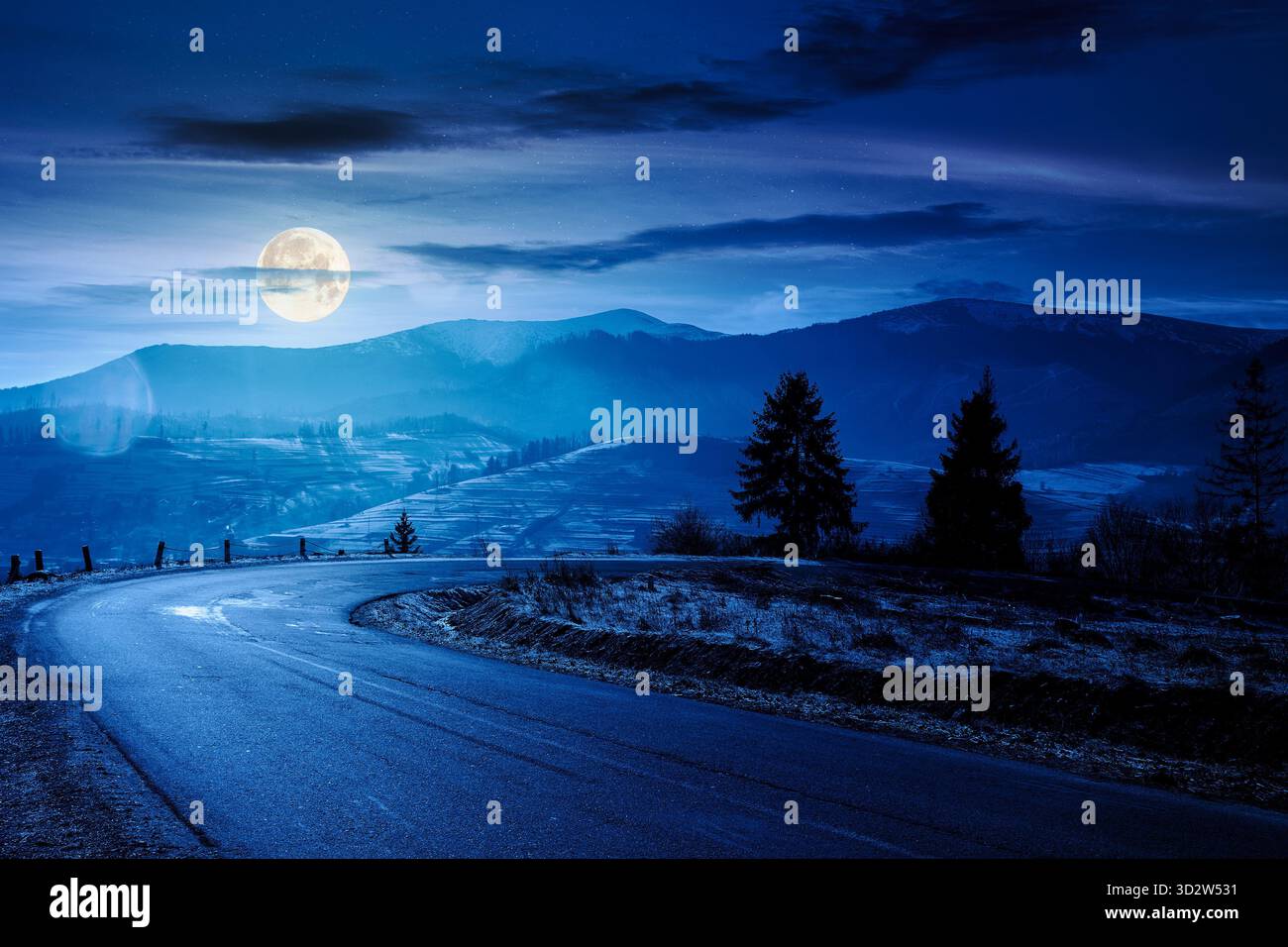 country road in mountains at night. beautiful countryside landscape in late autumn. fir trees on the roadside in full moon light. scenic view of blue Stock Photo