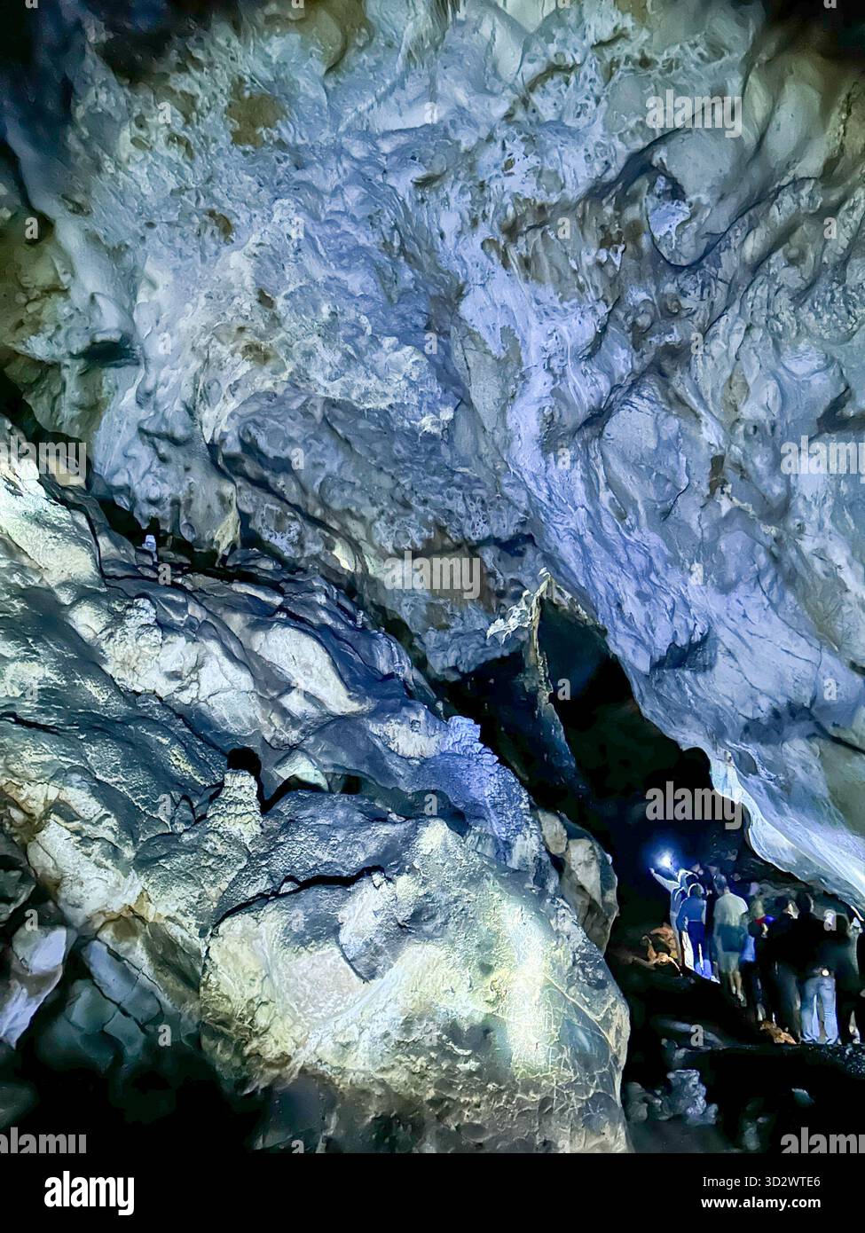 Visitors explore the stunning Ice Cave in Uvac Canyon, Serbia, illuminated by soft light revealing dramatic rock formations and textures. - Smartphone Captured Stock Image