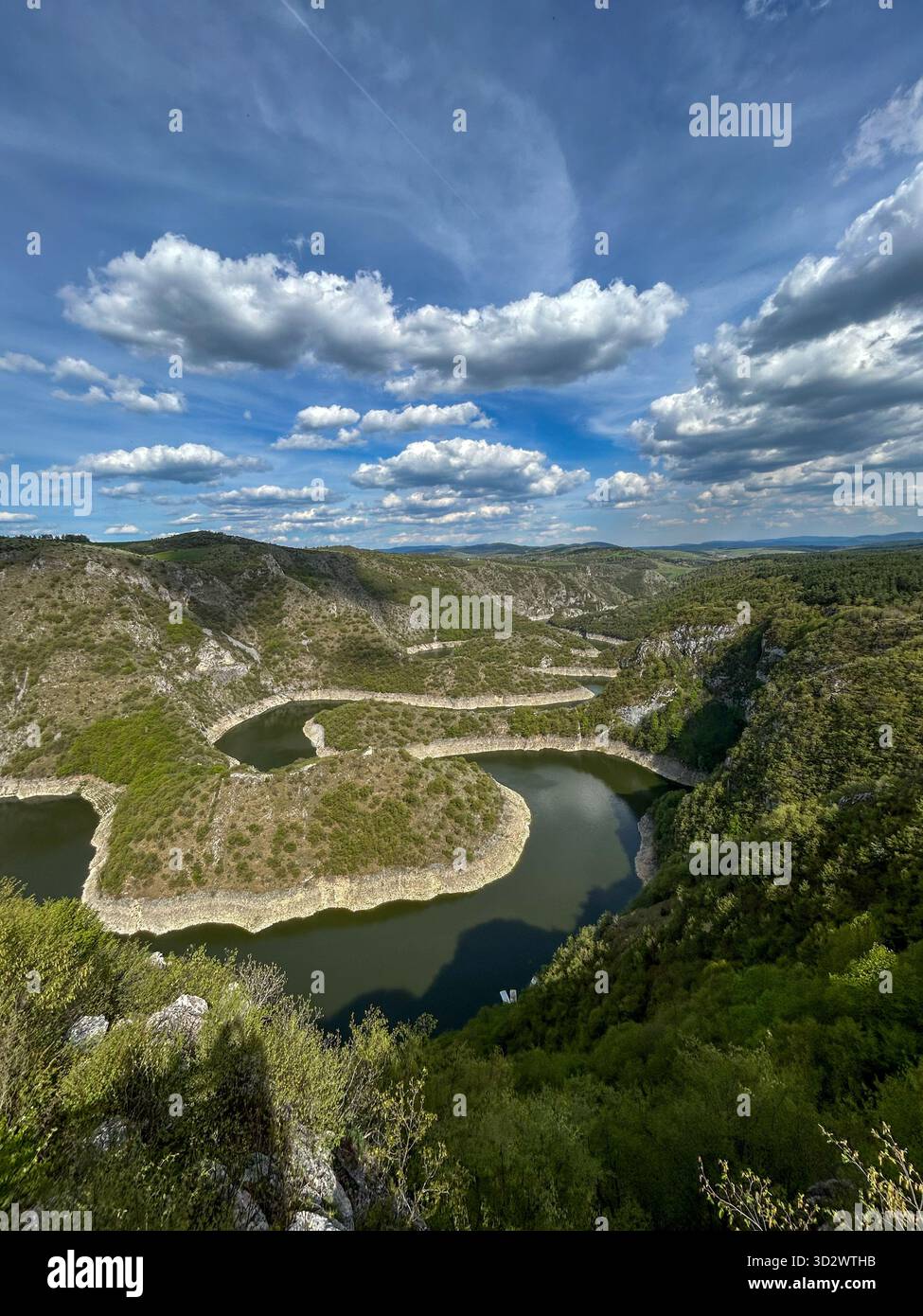 Aerial view of the winding Uvac River canyon in Serbia, surrounded by lush green hills and dramatic clouds on a sunny day. - Smartphone Captured Stock Image