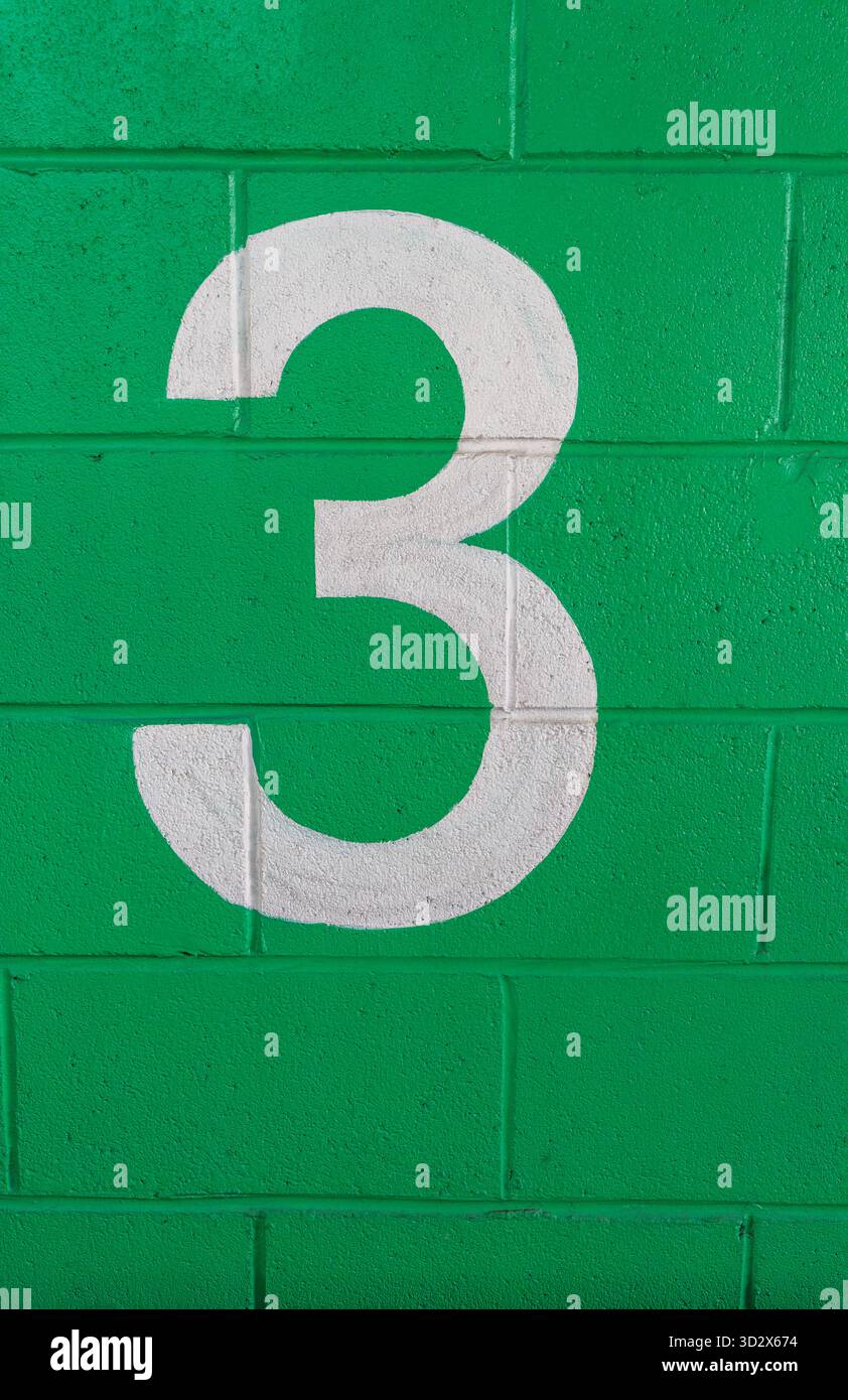 A white painted number 3 on a green brick wall Stock Photo