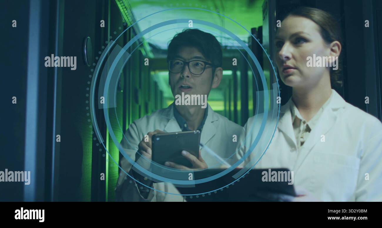 Two IT technicians projecting and analyzing 3D interface in hall, with server racks and tablets Stock Photo