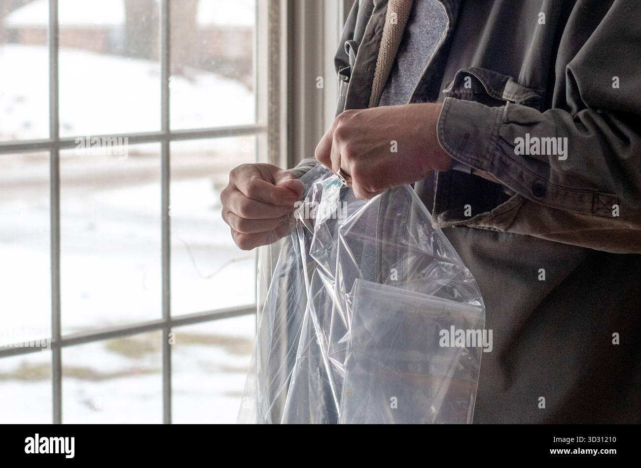 Hands unfold a large sheet of plastic for winter insulation around a large window Stock Photo
