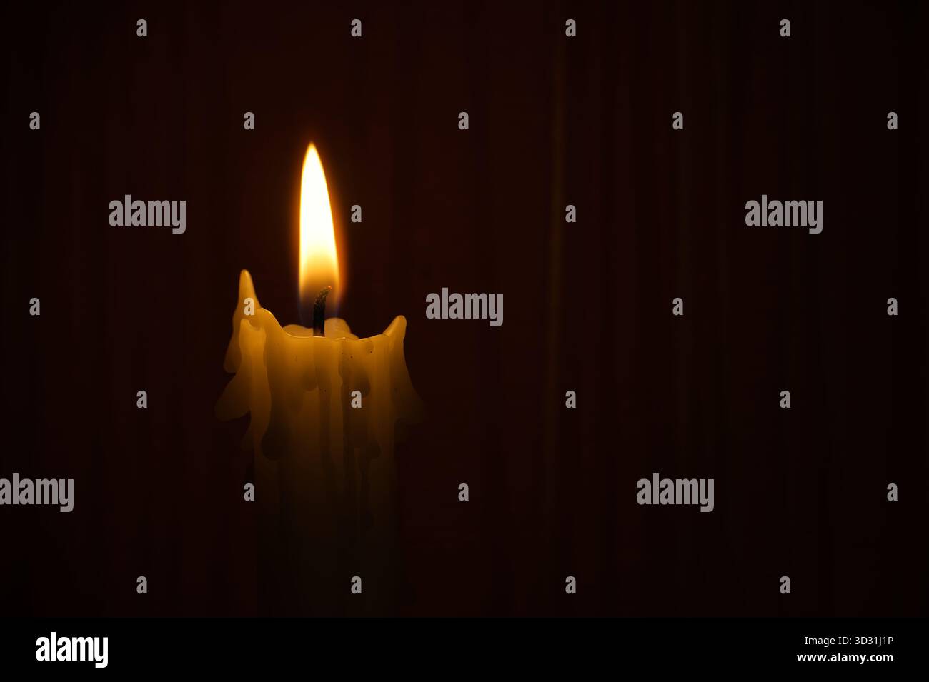 Solitary candle burns in dark setting, bright flame casting a soft ...