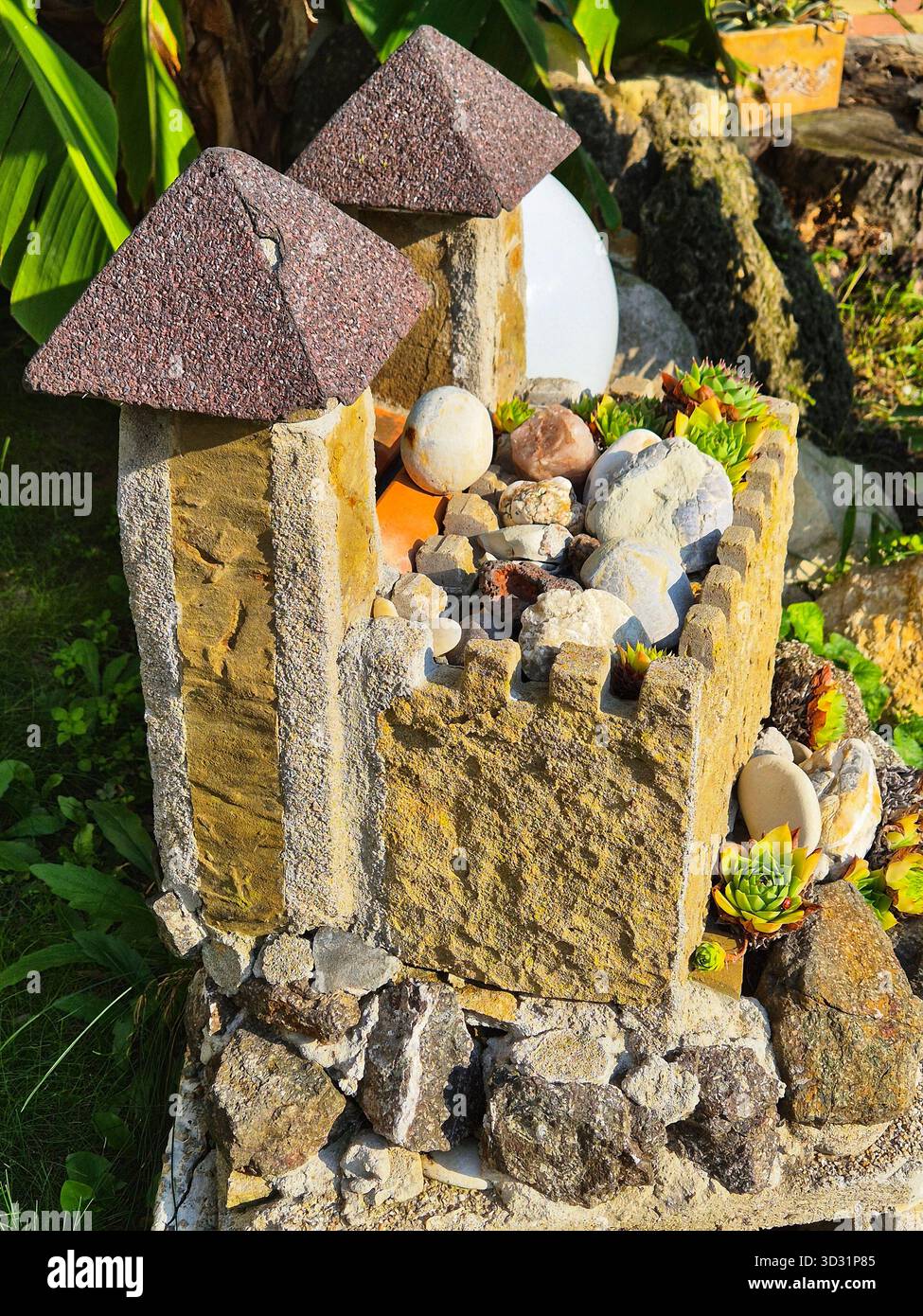 Miniature stone castle in the garden.Fairytale rock garden with pyramids. Garden decor made of stone and succulents. - Smartphone Captured Stock Image