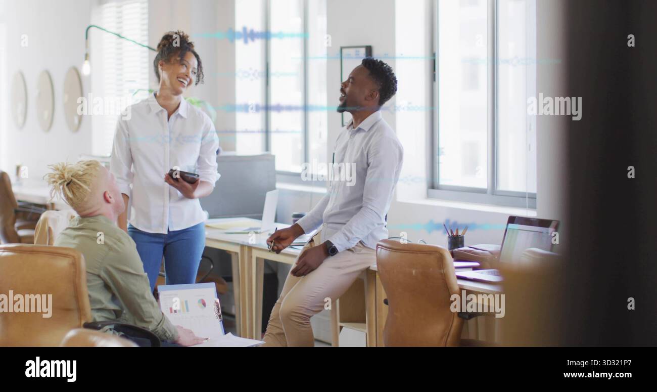 Collaborating professionals reviewing laptop charts and smartphone in open office with wooden desks Stock Photo