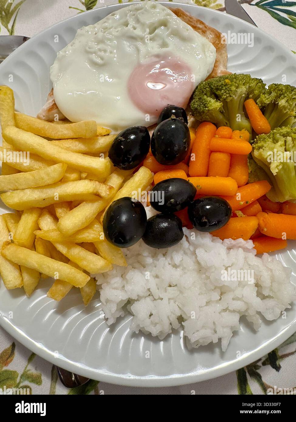 Plate of assorted food including fried egg, chicken, rice, fries, broccoli, carrots, and black olives. - Smartphone Captured Stock Image