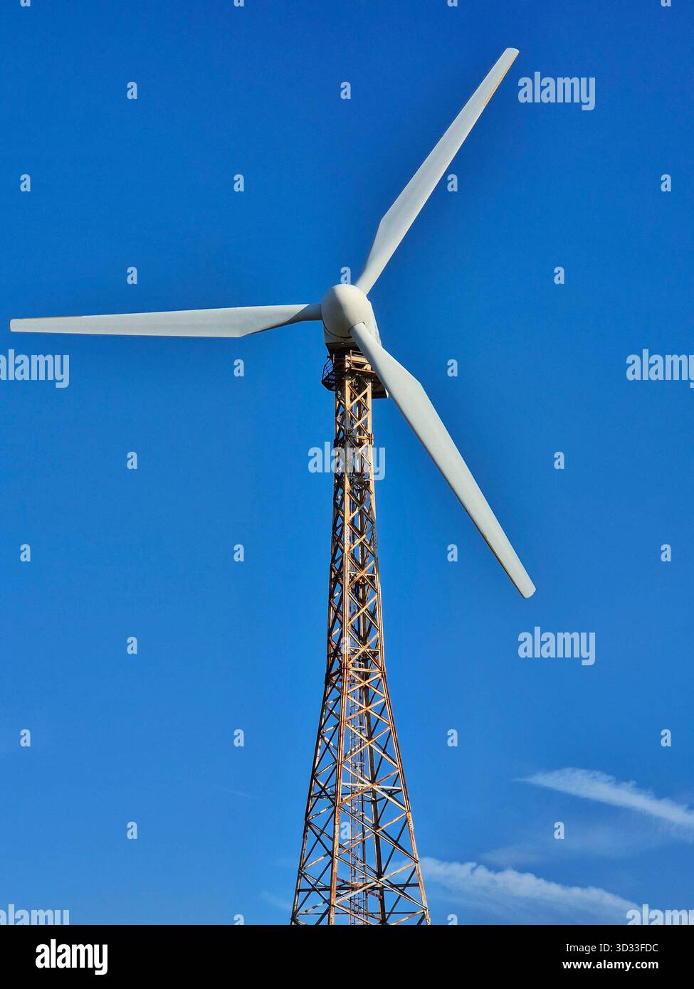 Vertical shot of a wind turbine. A tall, open lattice tower supports a three-bladed rotor - Smartphone Captured Stock Image