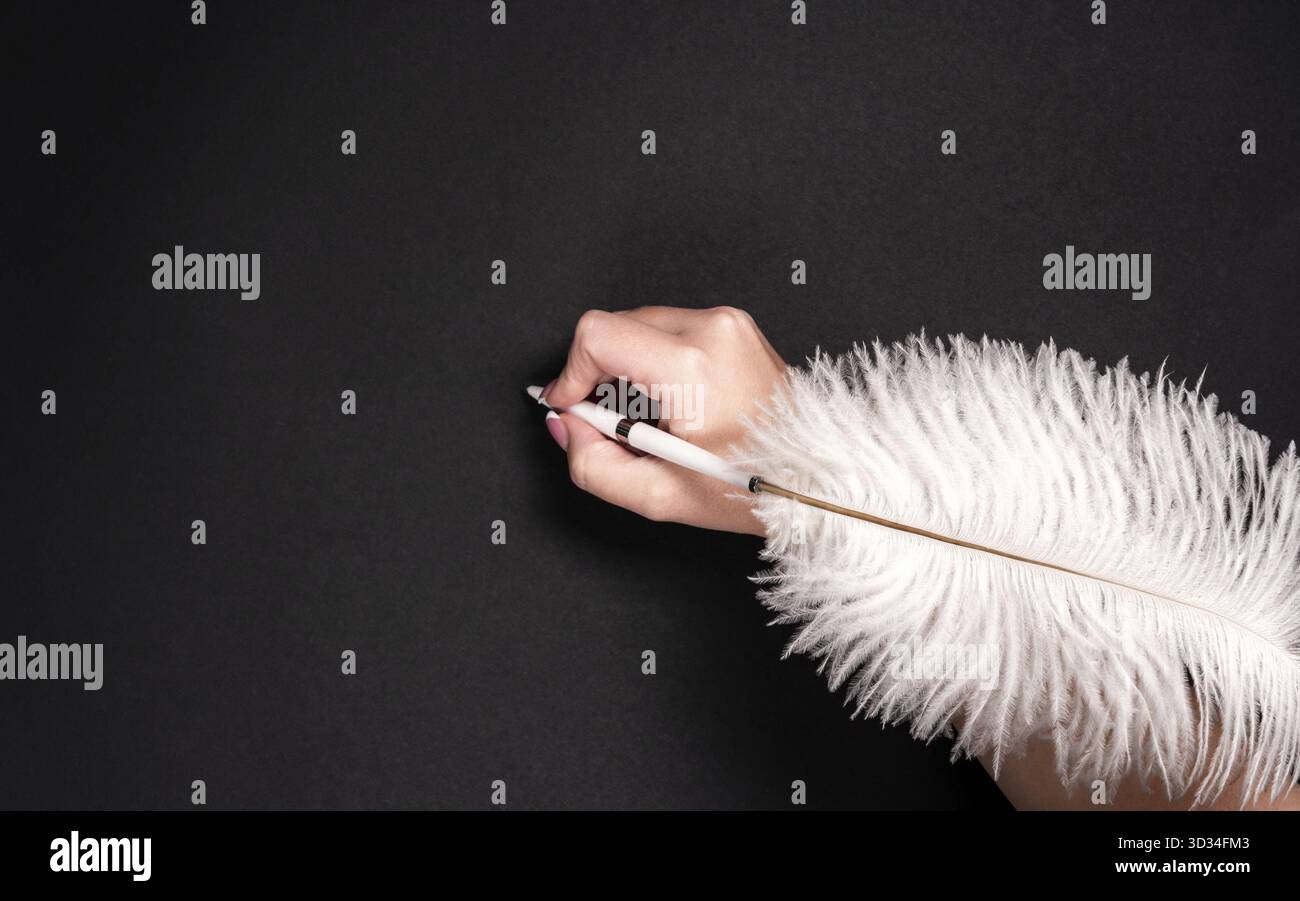 Female hand holding feather pen over black background Stock Photo