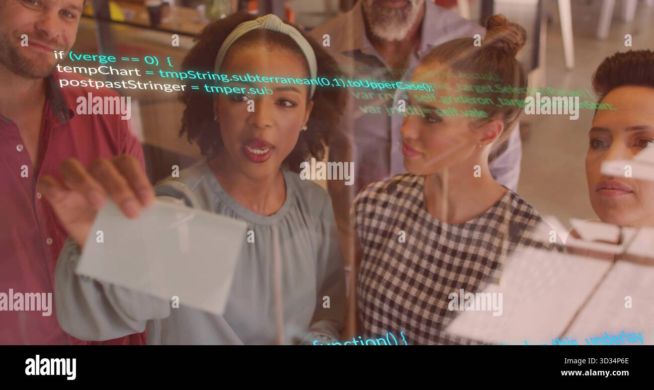 Collaborating team placing index cards on transparent board at open-plan office, with code snippets Stock Photo