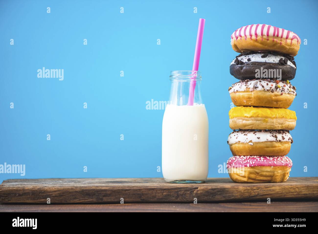 Milk bottle and stack of donuts on wooden board, negative space bright background Stock Photo