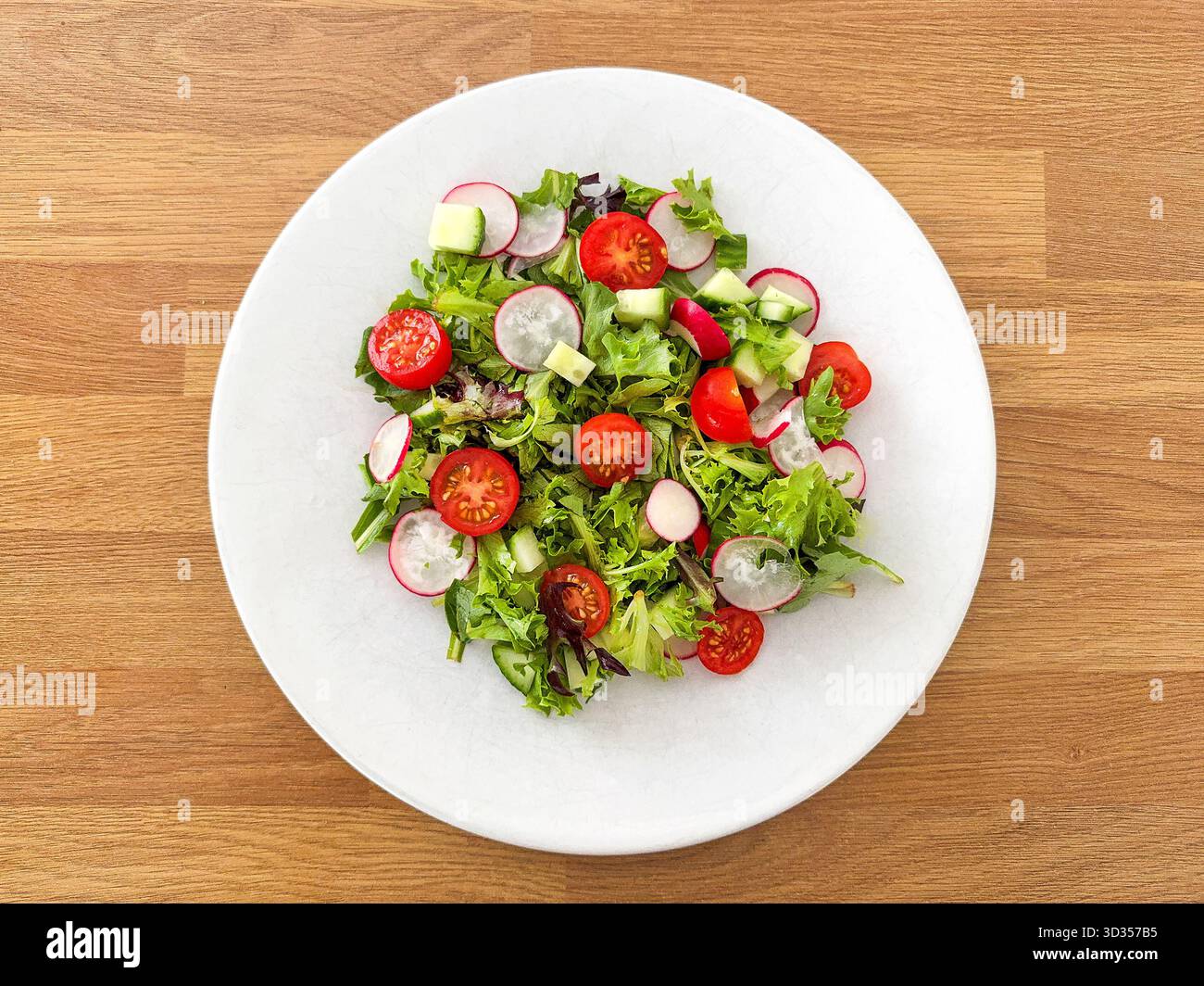 Simple salad with lettuce, tomatoes, cucumber and radish on a white plate on a wooden table. - Smartphone Captured Stock Image