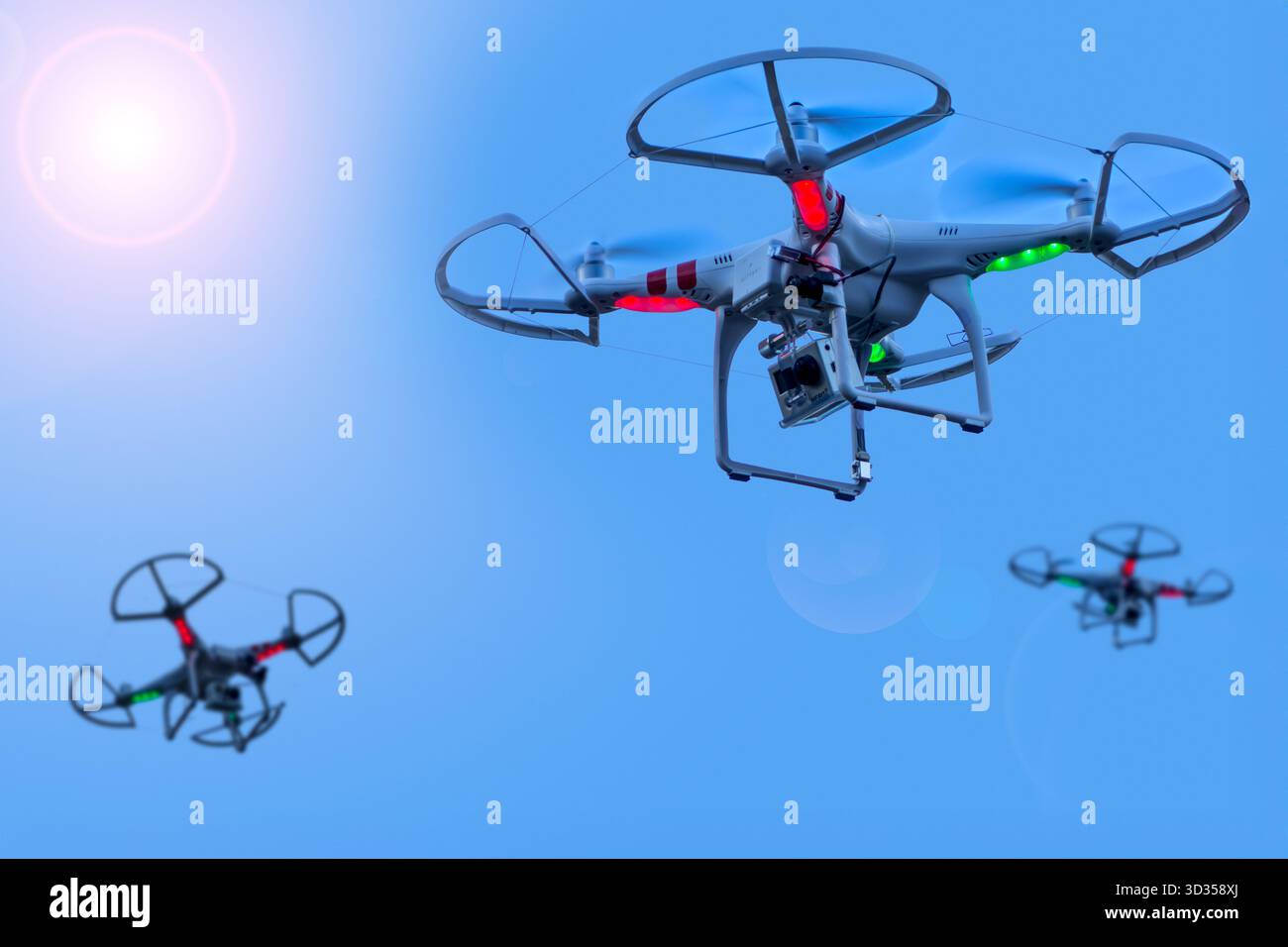 Three miniature quadcopter drones / teleoperated unmanned aerial vehicles / UAV equipped with cameras for aerial photography in flight in group Stock Photo