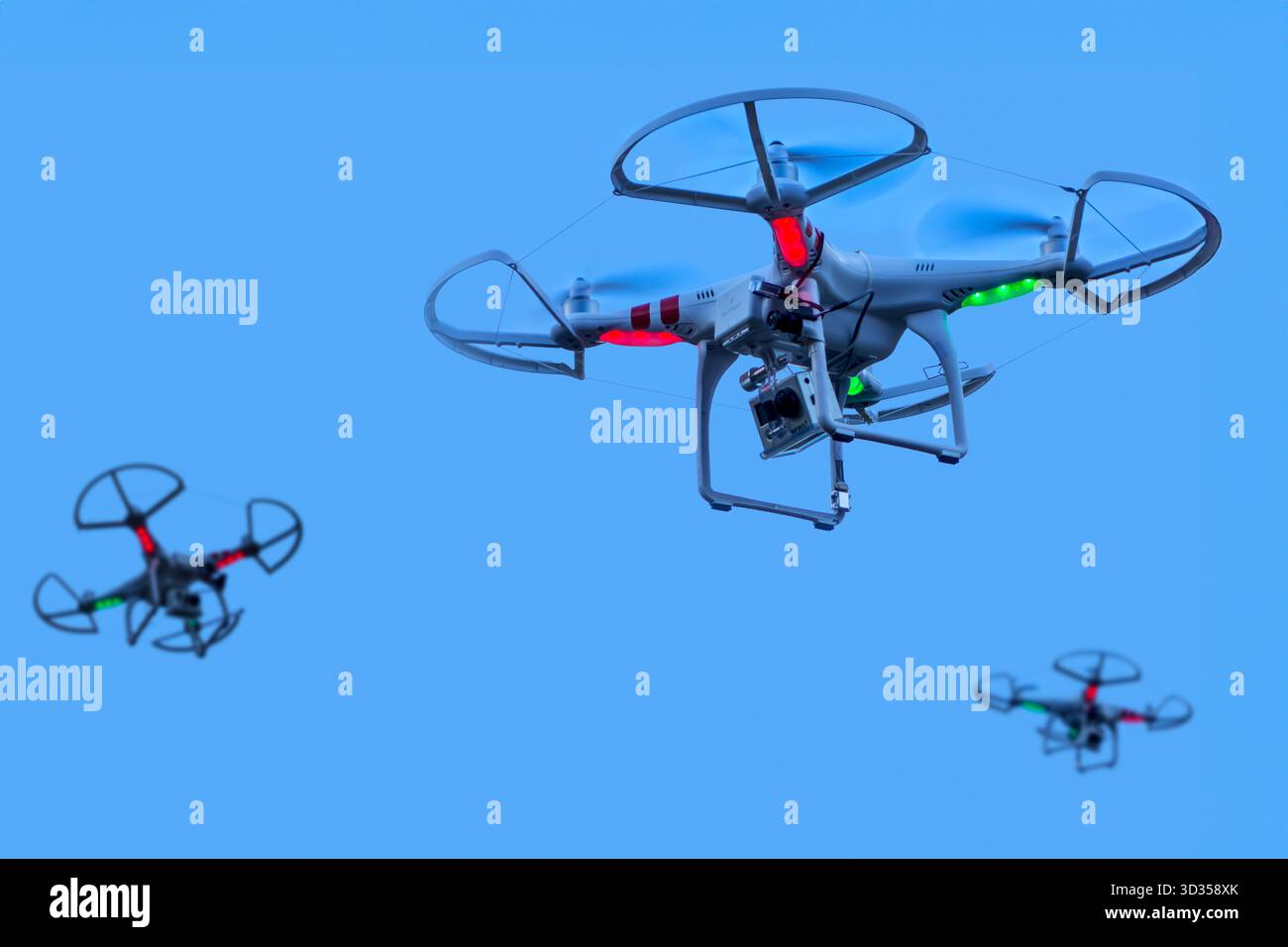 Three miniature quadcopter drones / teleoperated unmanned aerial vehicles / UAV equipped with cameras for aerial photography in flight in group Stock Photo