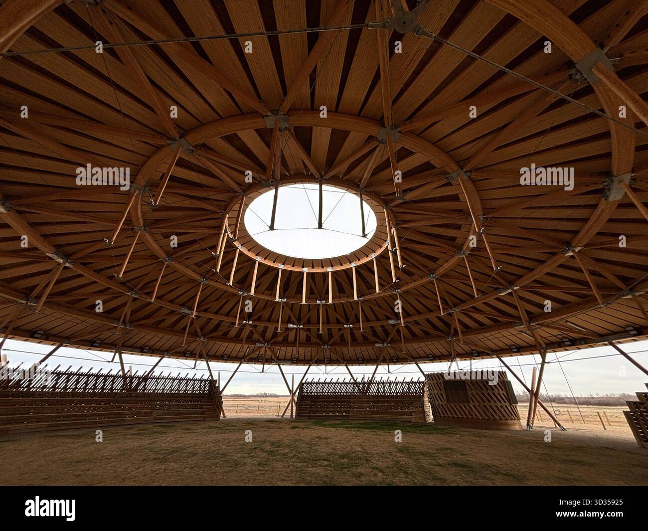 Timber amphitheatre with sweeping wooden roof and tiered seating on an indigenous reserve, set against vast prairies, symbolizing sustainable design. - Smartphone Captured Stock Image