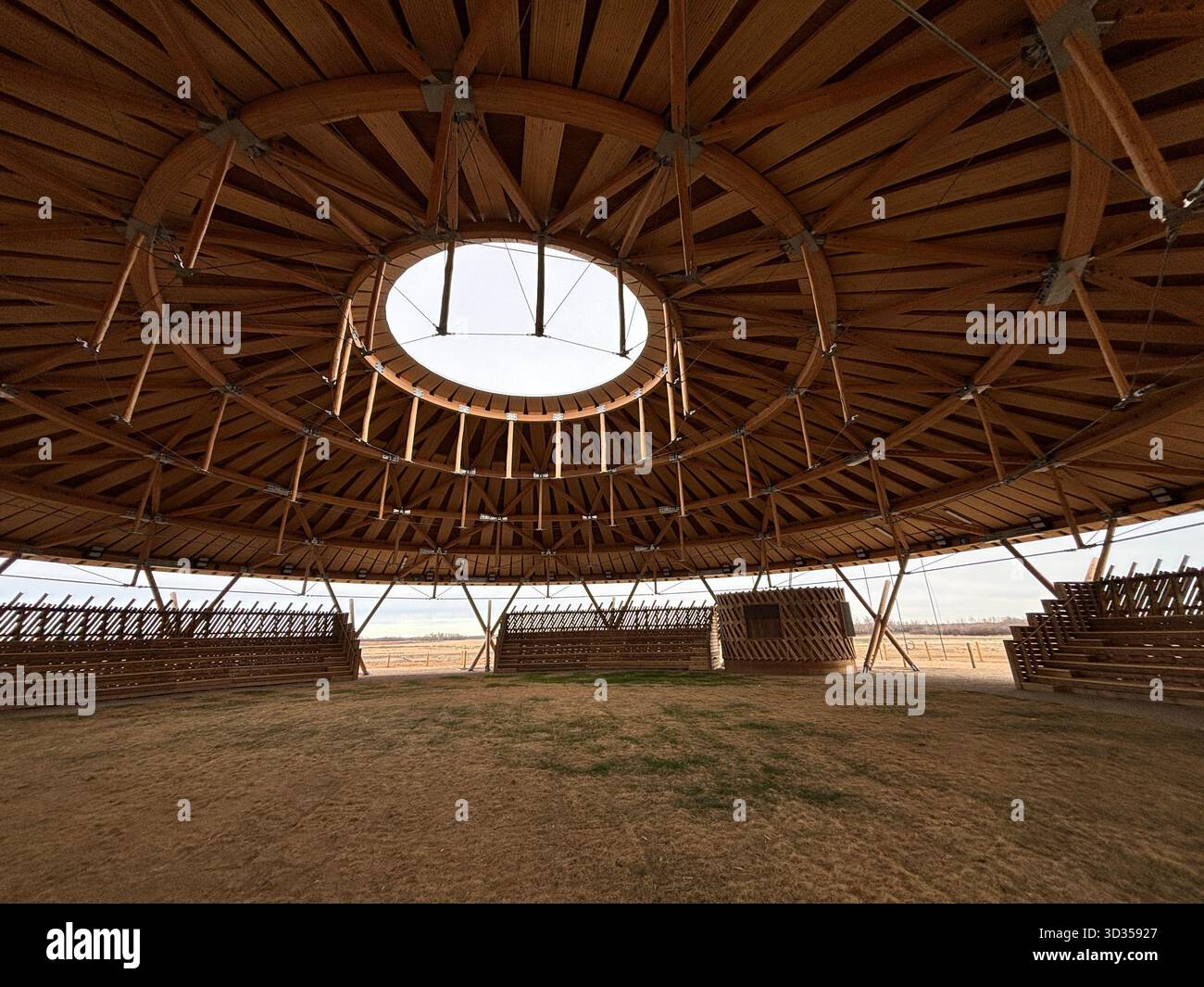 Timber amphitheatre with sweeping wooden roof and tiered seating on an indigenous reserve, set against vast prairies, symbolizing sustainable design. - Smartphone Captured Stock Image