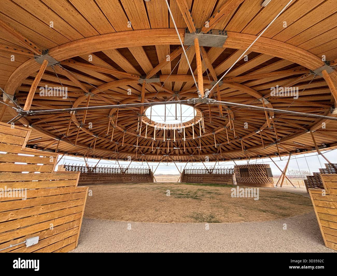 Timber amphitheatre with sweeping wooden roof and tiered seating on an indigenous reserve, set against vast prairies, symbolizing sustainable design. - Smartphone Captured Stock Image