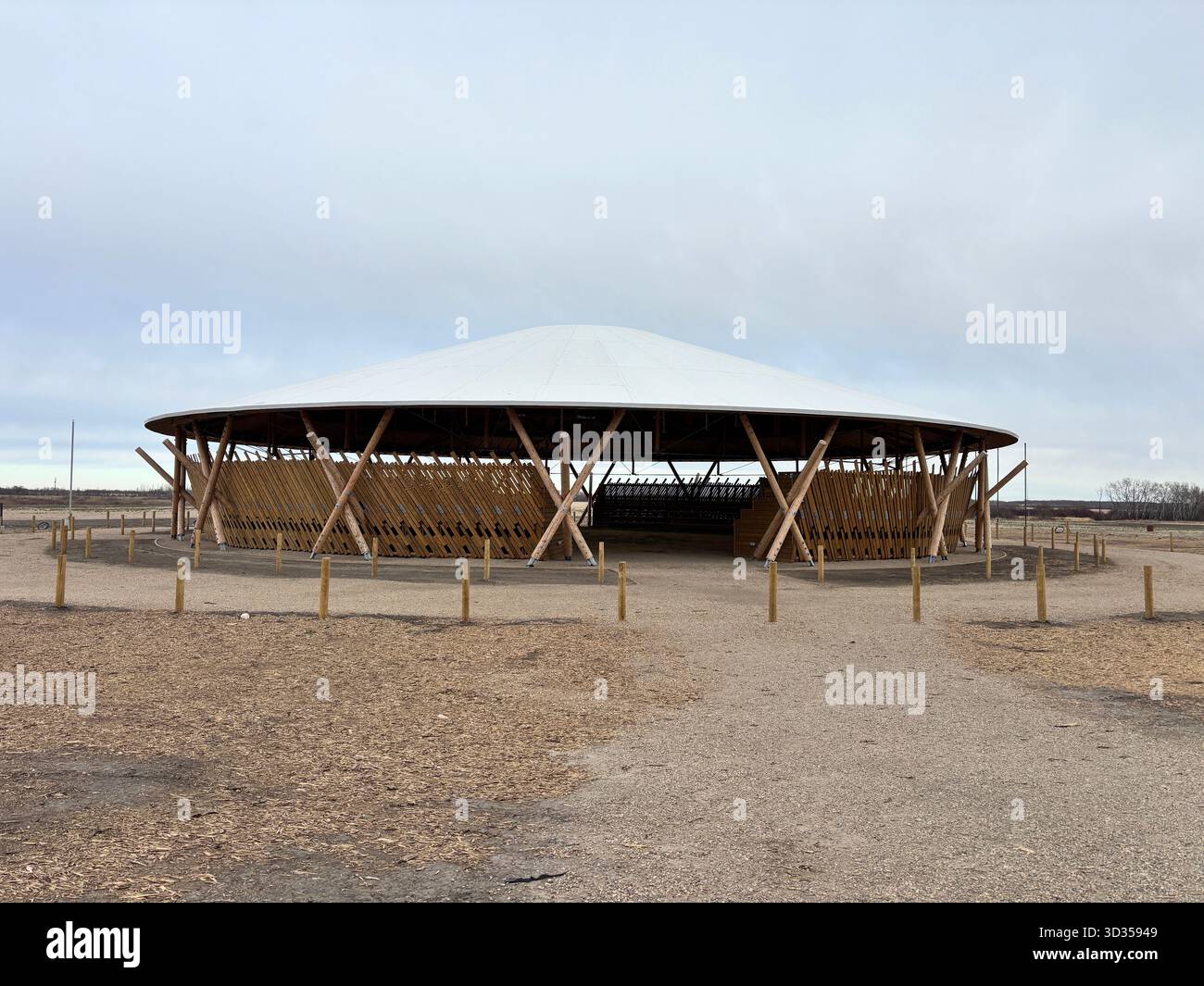 Timber amphitheatre with sweeping wooden roof and tiered seating on an indigenous reserve, set against vast prairies, symbolizing sustainable design. - Smartphone Captured Stock Image