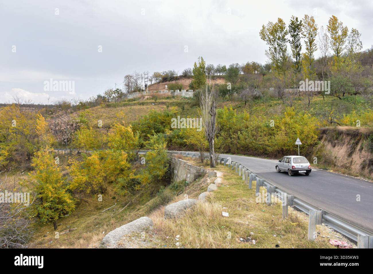 A vehicle moves through the colorful fall foliage during an autumn season in Budgam, about 50kms from Srinagar, the summer capital of Jammu and Kashmir. Autumn, locally known as Harud, is a season of harvesting in Kashmir with trees changing their colours while the day light hours become shorter as winter approaches. Stock Photo