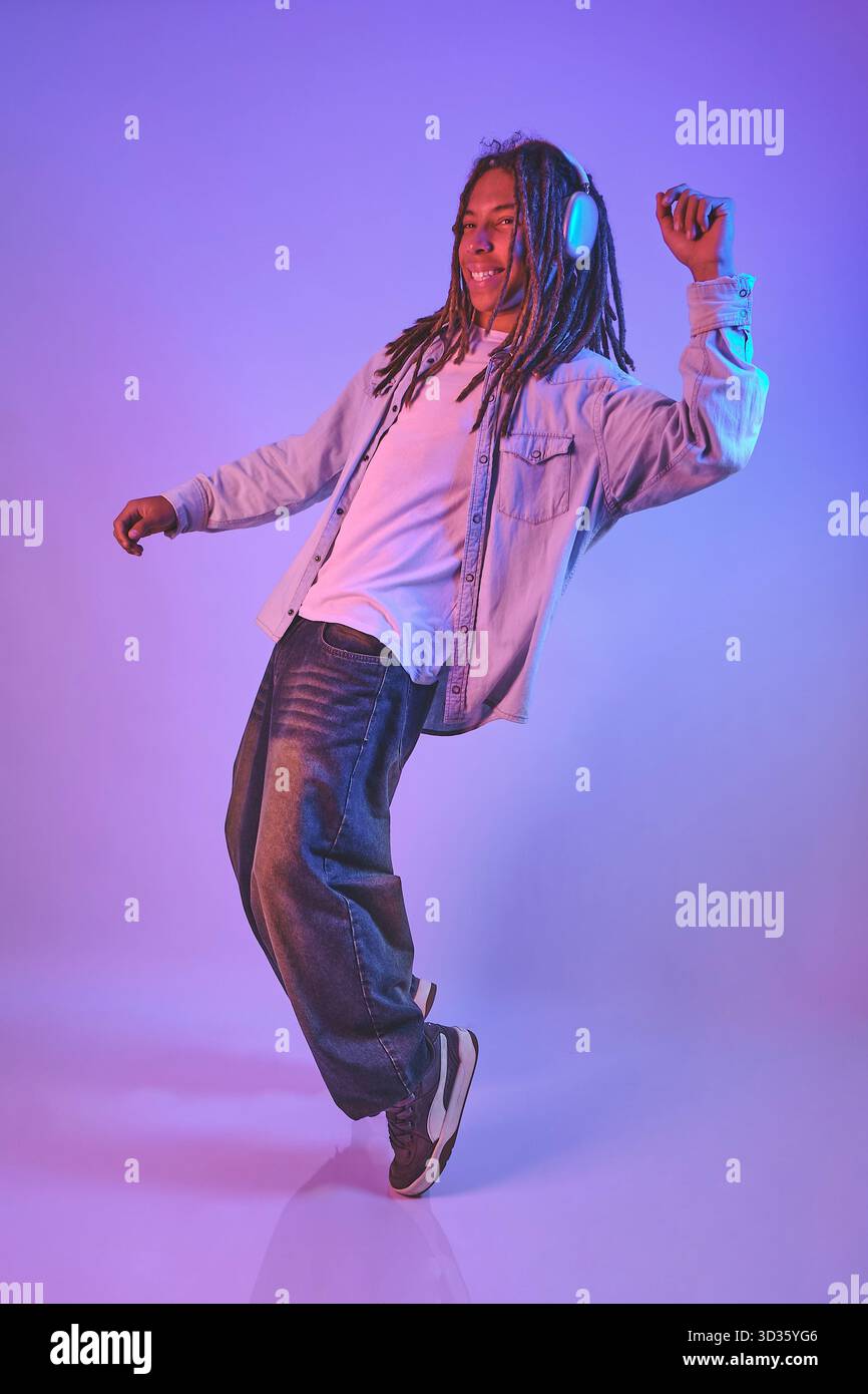 Young man enjoying music with headphones while dancing in neon light Stock Photo