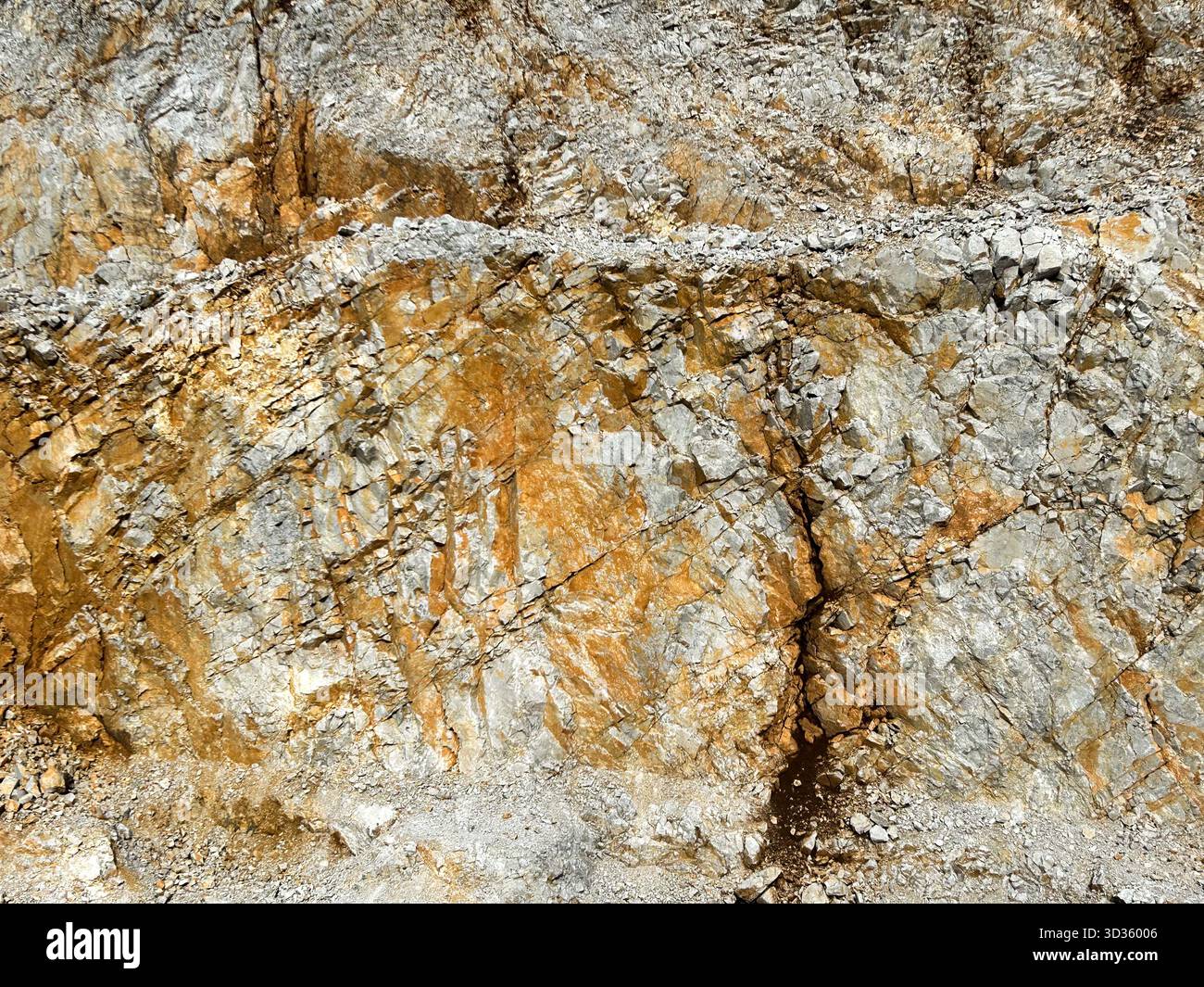 Close-up of a rugged rock surface showing natural mineral layers and textures in shades of gray, brown, and gold, revealing geological formations. - Smartphone Captured Stock Image