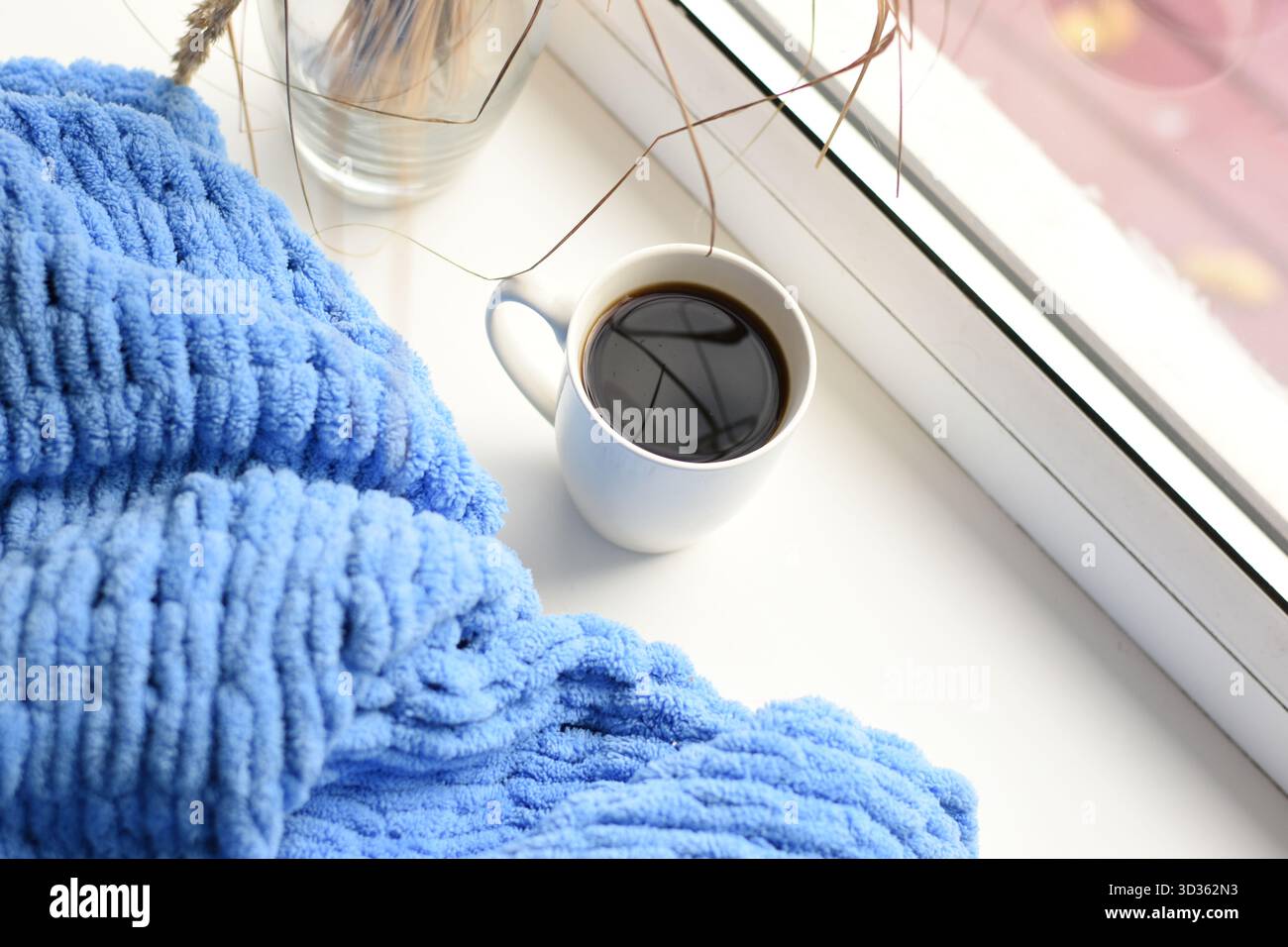 Top view of coffee cup on white windowsill with blue knitted blanket, bright cozy scene. Stock Photo