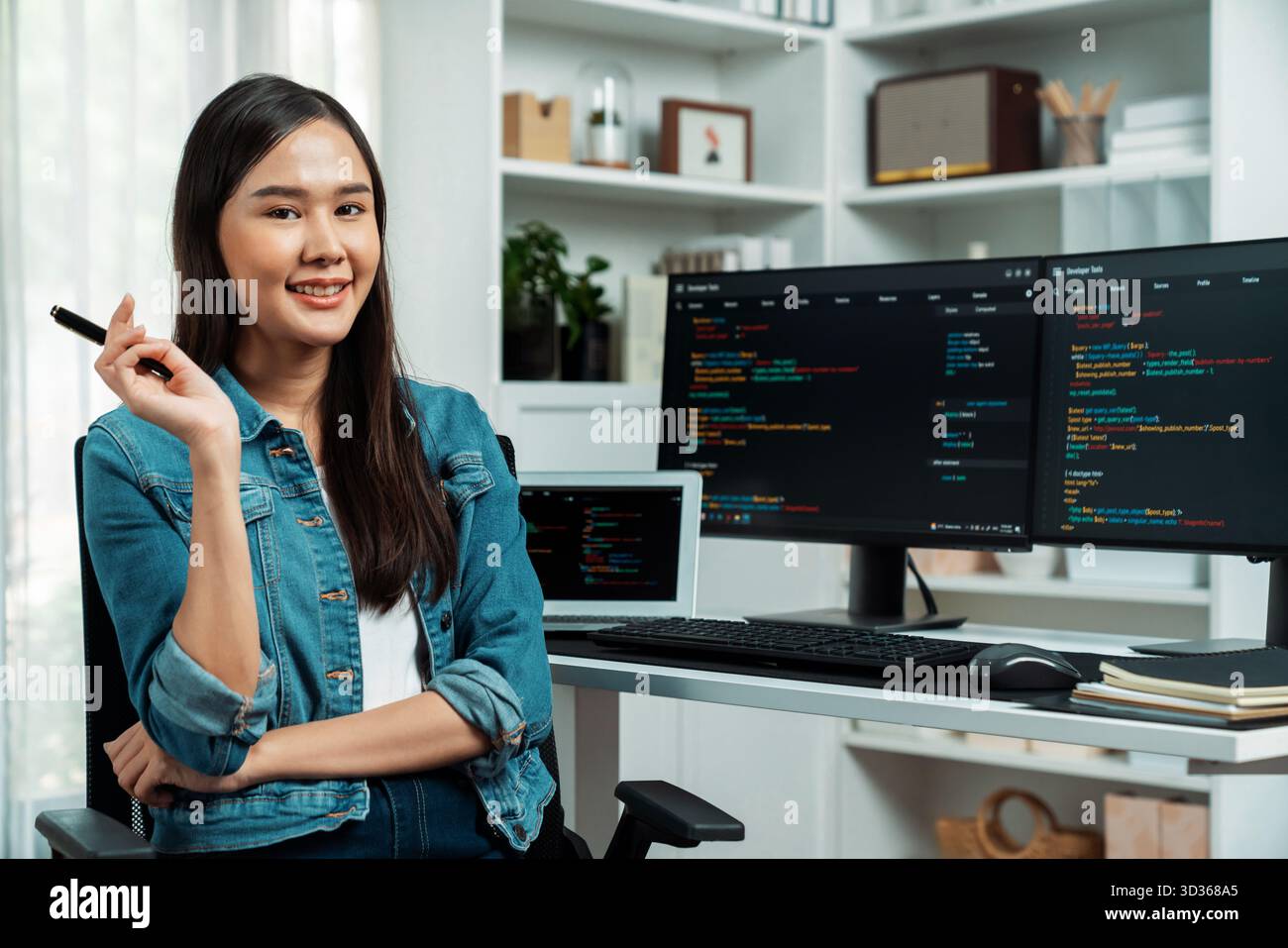 Young Asian in IT developer looking at camera to present with online information on pc with coding program data application, wearing jeans shirt Stock Photo