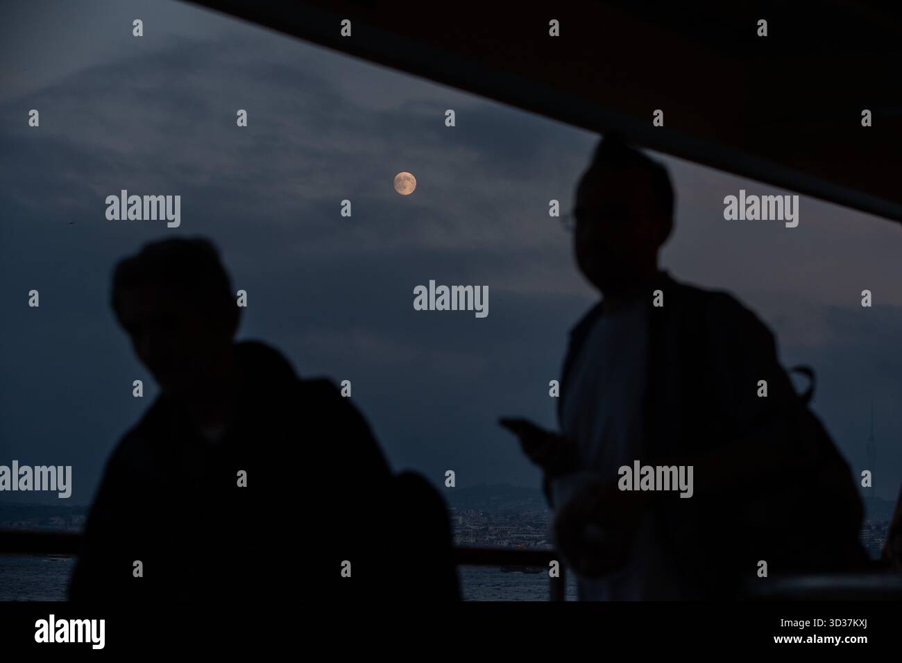 Istanbul, Turkey. 04th Nov, 2025. The silhouettes of two passengers on a city lines ferry in Istanbul seen with a full moon in the background. Credit: SOPA Images Limited/Alamy Live News Stock Photo