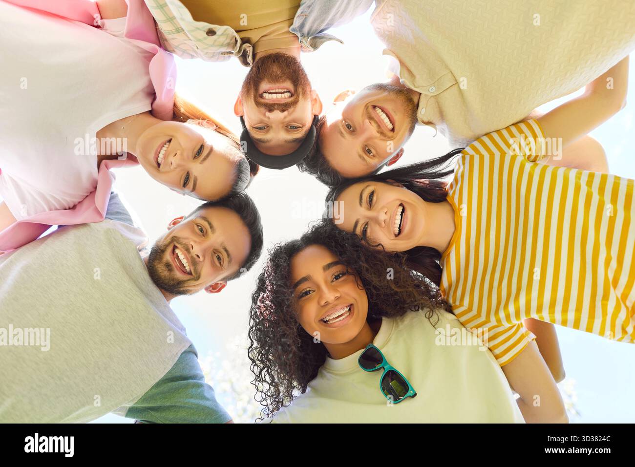 Friends together, group of young adults standing closely together in circle, looking downwards Stock Photo
