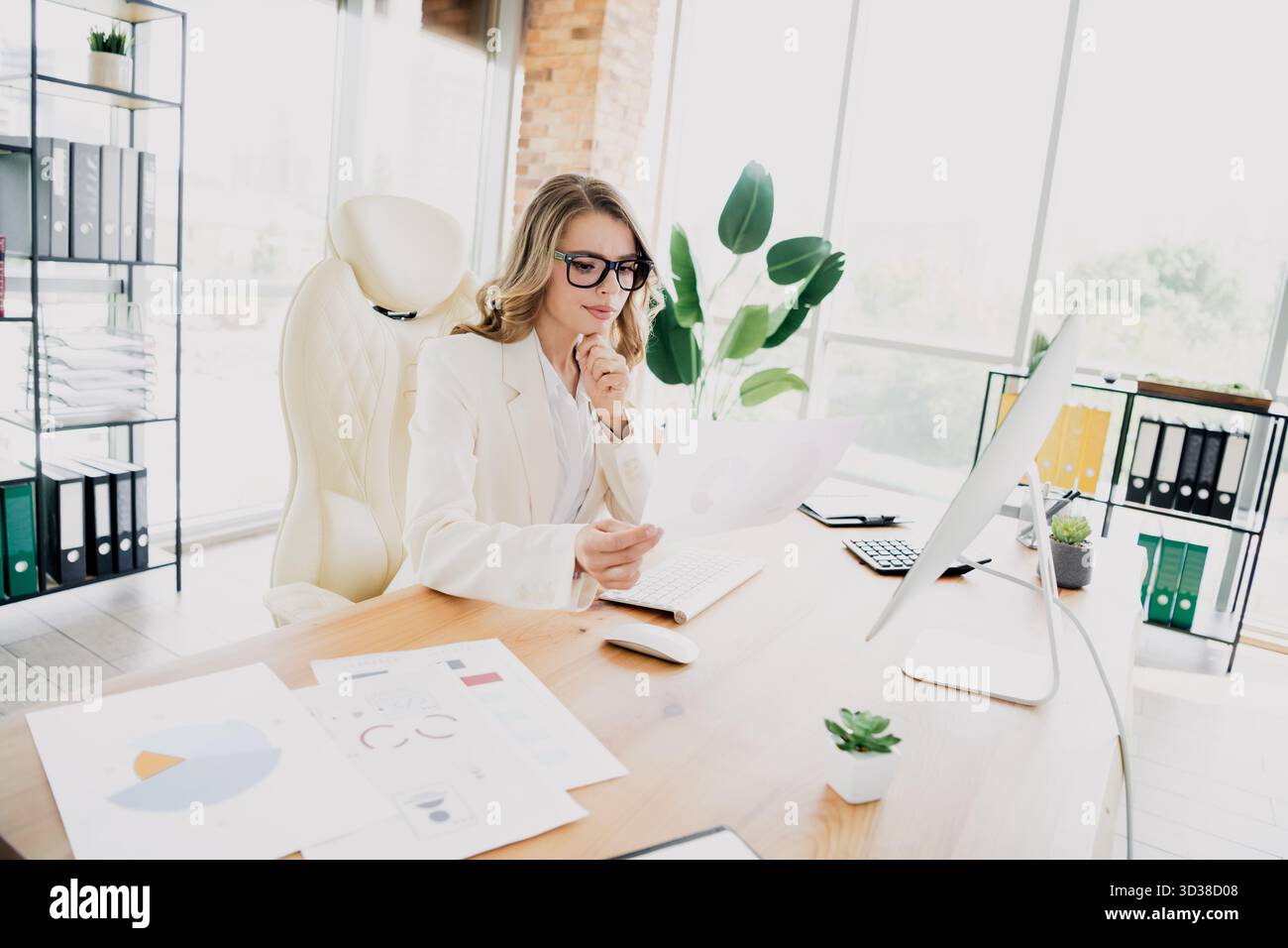 Confident young businesswoman analyzing financial reports in a bright modern office setting for strategic decision making Stock Photo