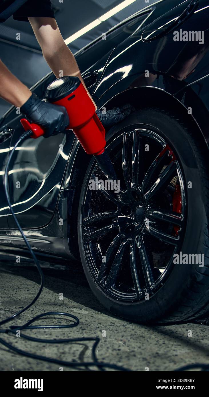 Worker drying car wheel with red air blower during detailing process ...