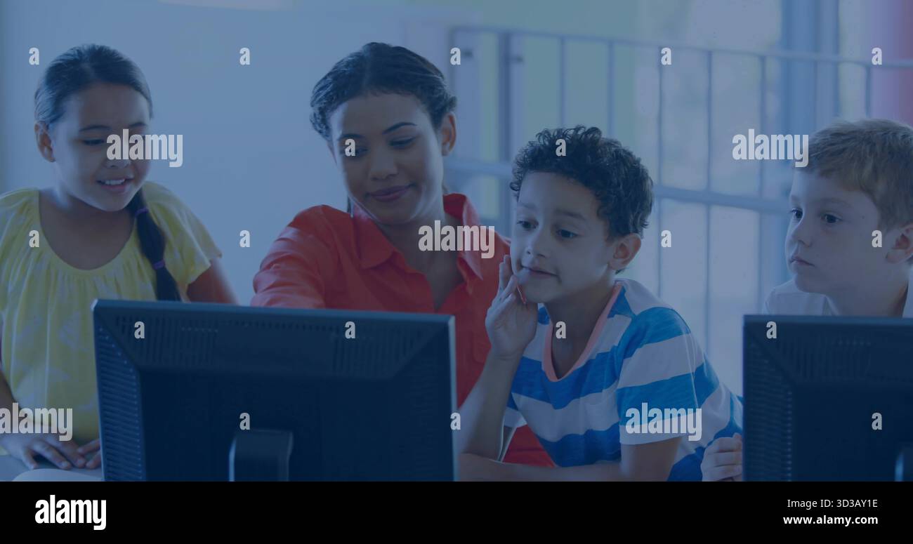 Female instructor guiding three schoolchildren in computer lab classroom, with desktop computers Stock Photo