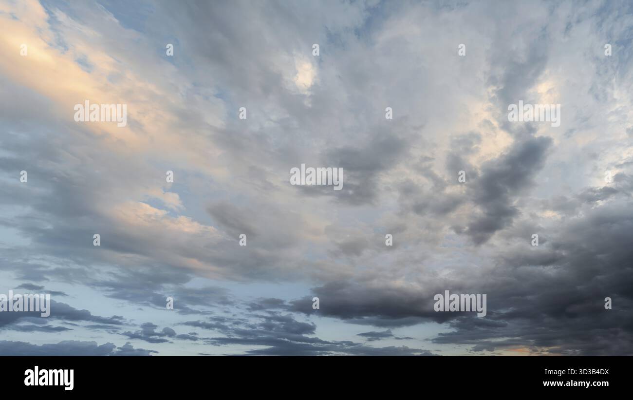 Evening sky with dramatic clouds in various shades and textures. A large panorama of the sky with beautiful clouds illuminated by soft sunlight Stock Photo