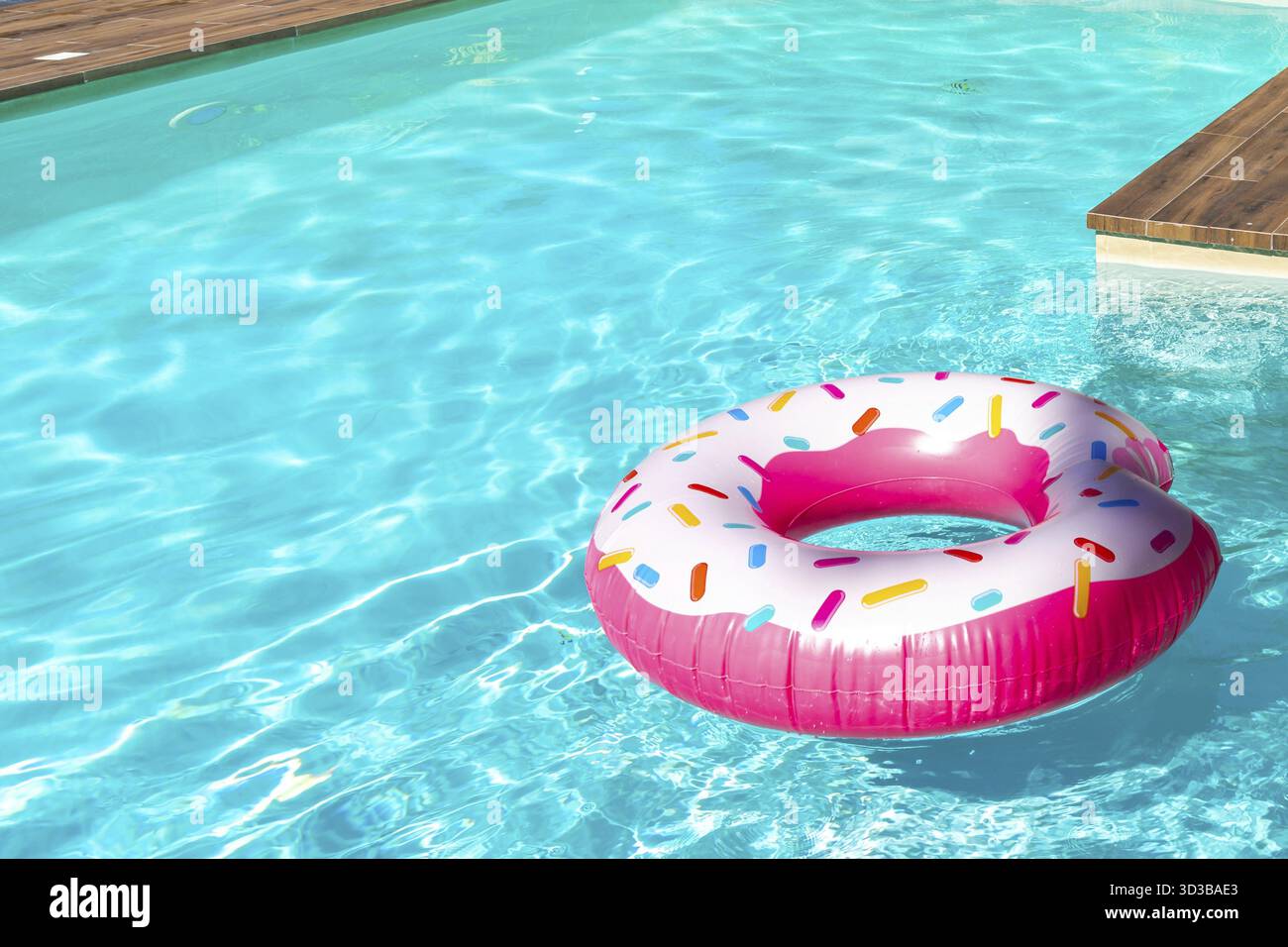 Pink donut-shaped inflatable float in turquoise swimming pool with ...