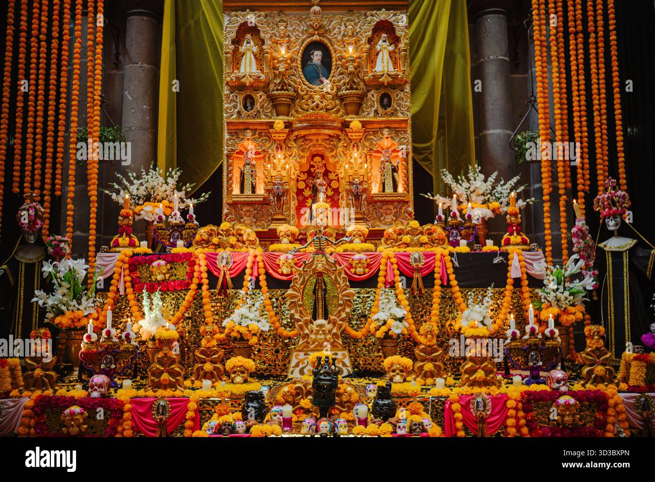 Spectacular front view of a multi-level Day of the Dead altar, decorated with marigold, figures, candles, and a golden retablo backdrop. Stock Photo