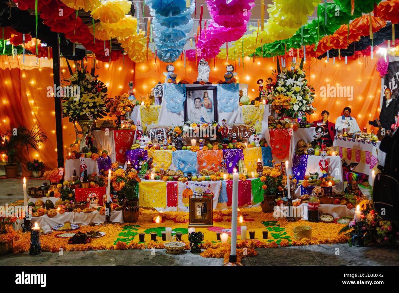 Wide view of a large, multi-level Day of the Dead altar decorated with papel picado, candles, flowers, and a photograph of the deceased. Stock Photo