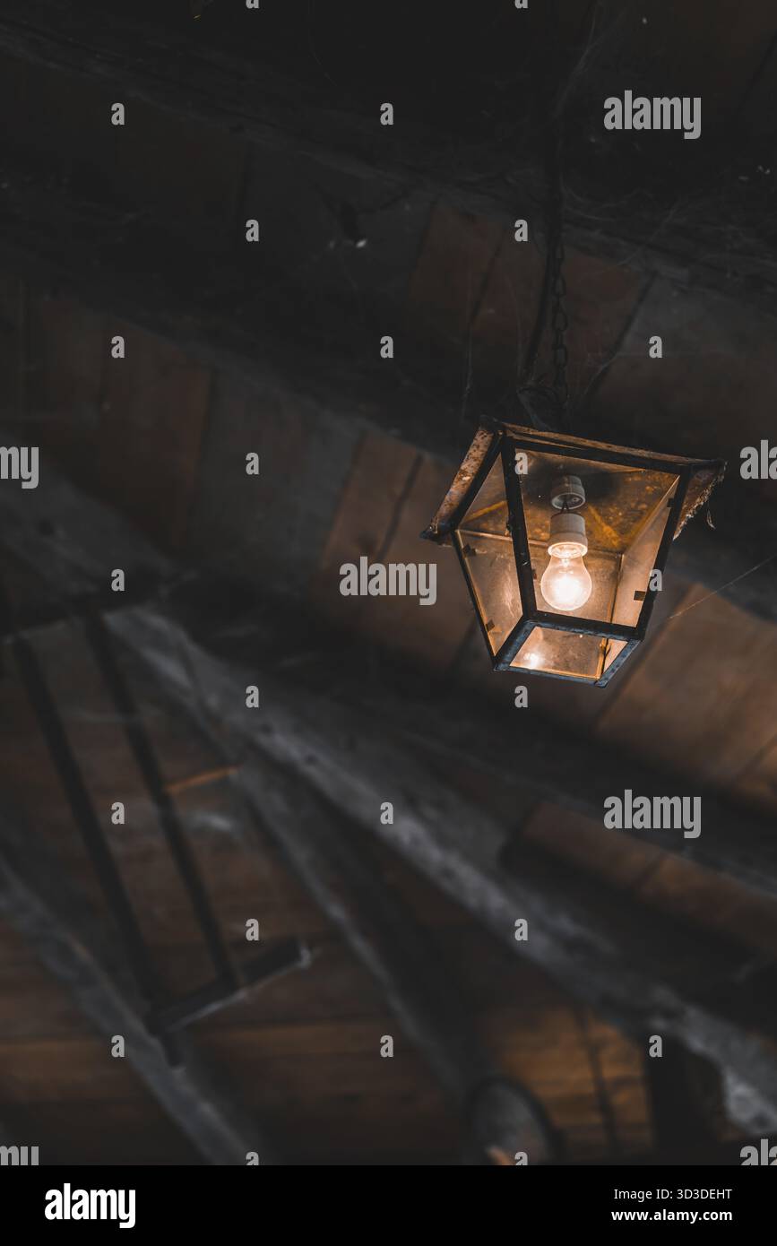Old lamp covered in spider web hanging from the ceiling in an old farm ...