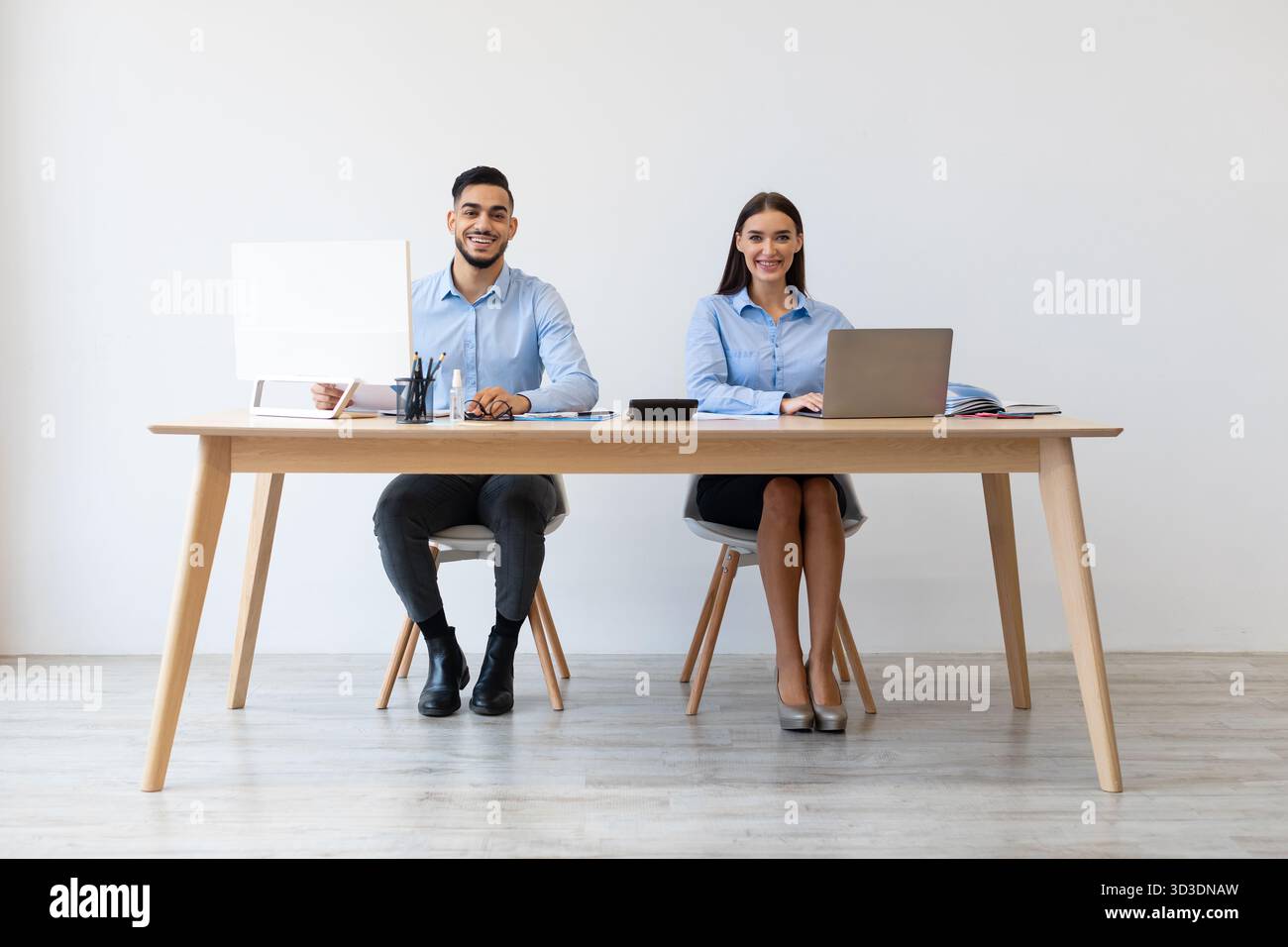 Colleagues Enjoying Teamwork at Office Desk While Using Laptops and Smiling for Camera Stock Photo
