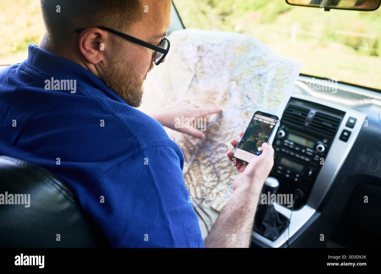 Mapguide Backseat Driver Man tourist sits in driver's seat of car, holding paper map and using ...