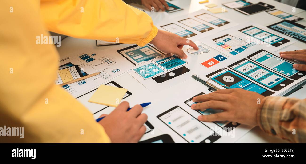 A vibrant workspace bustling with designers collaborating on a mobile app prototype, showcasing user interface wireframes, tools, and creative Stock Photo