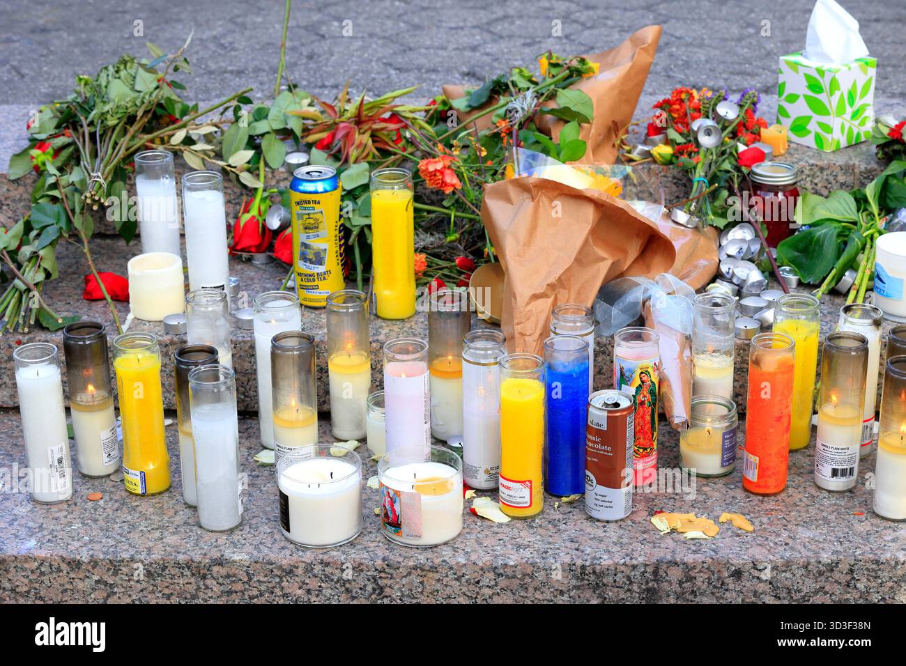 Flowers and religious candles, prayer candles, and beverages at a makeshift sidewalk street memorial Stock Photo
