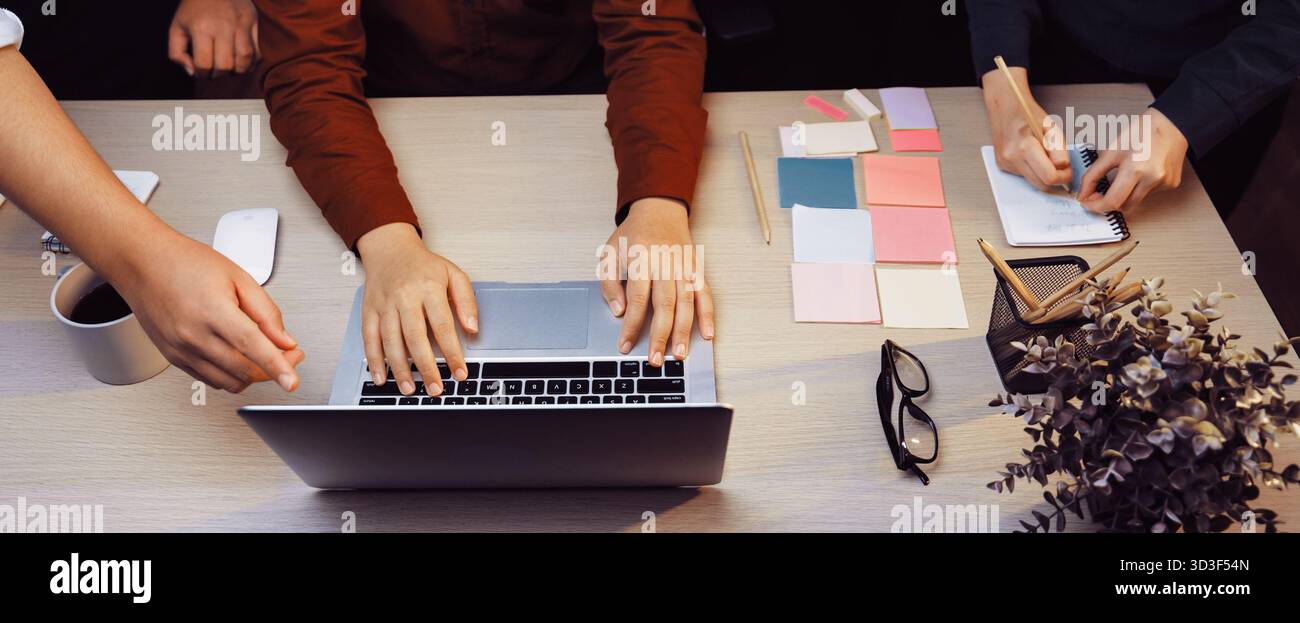 A dynamic workspace featuring a laptop and vibrant sticky notes, highlighting hands of individuals collaborating in a creative brainstorming session Stock Photo