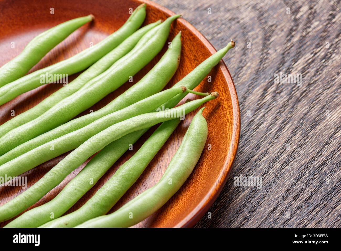 Closeup view of fresh green beans on wooden plate Stock Photo