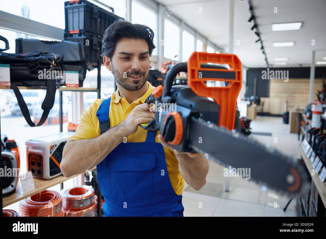 Worker is standing in a store holding a chainsaw tool Stock Photo