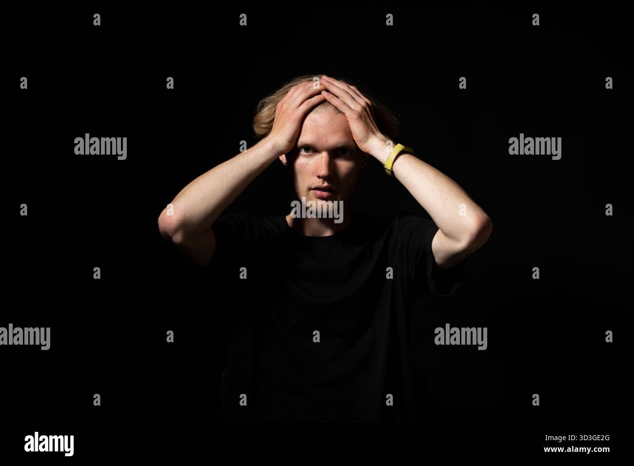 Shocked man in black shirt holding head with both hands in low key dramatic portrait Stock Photo