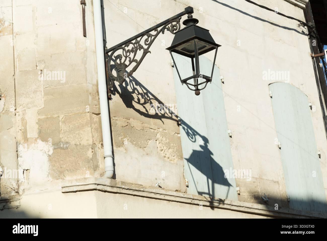 The late afternoon sun casts a shadow of a street  lamp on an old building in Arles France Stock Photo