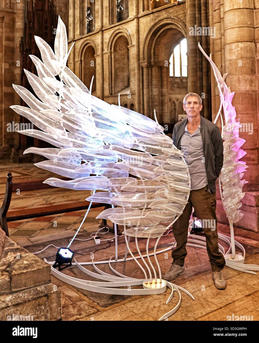 A striking glass wing sculpture, 'Solace' has gone on display at Peterborough Cathedral.Created by artist Layne Rowe (pictured), and standing at 10 feet high, Solace is a pair of shimmering glass wings, symbolising freedom, fragility, strength, and protection. Created from more than 100 individually hot-sculpted glass feathers, each feather features fine white canework to evoke the light, flowing nature of real wings. The iron framework and subtle lighting bring the piece to life, casting an ethereal glow. 'Solace' glass wing sculpture at Peterborough Cathedral, Peterborough, Cambridgeshire, Stock Photo